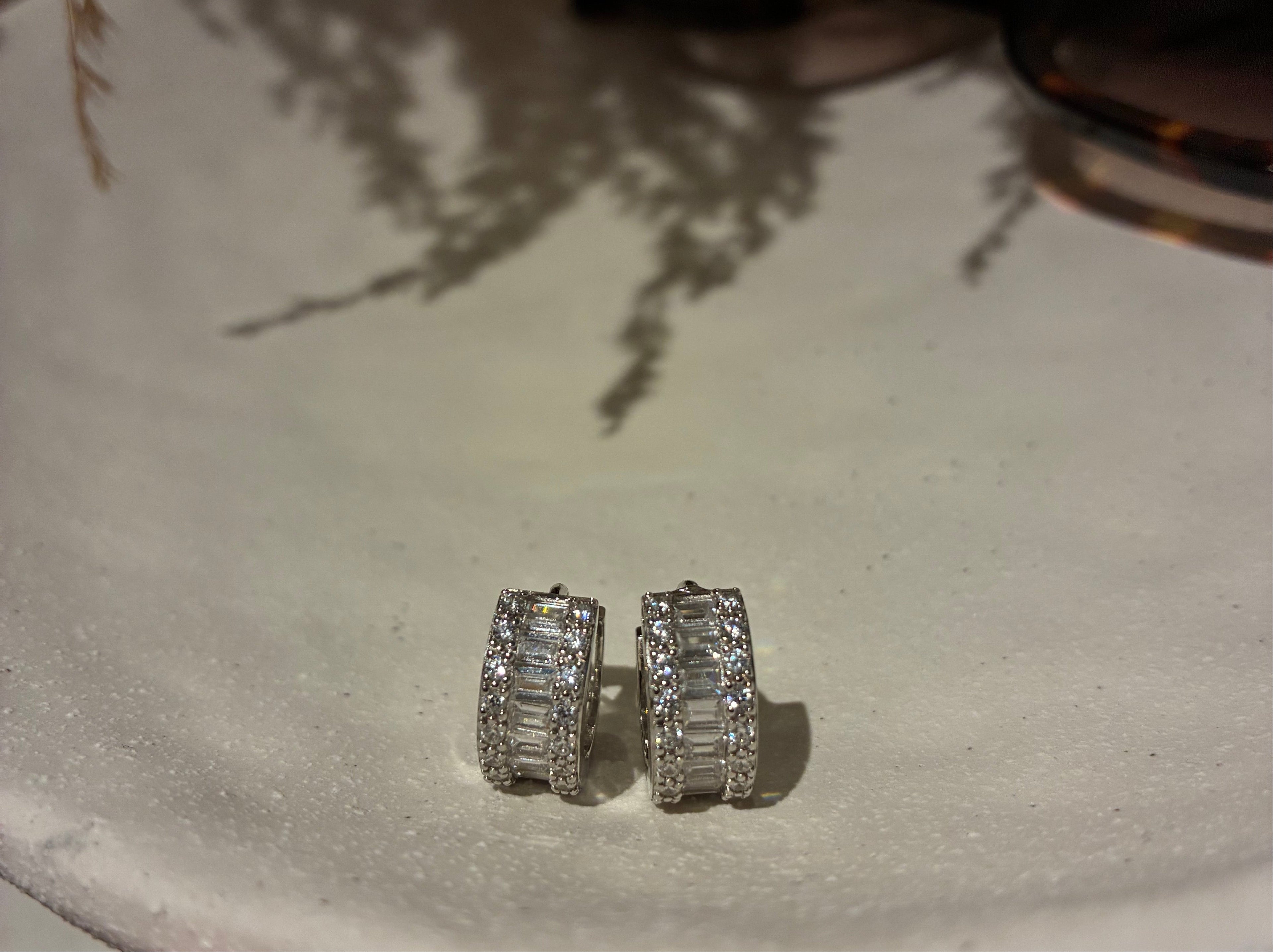 Silver earrings on a textured white surface with a blurred background